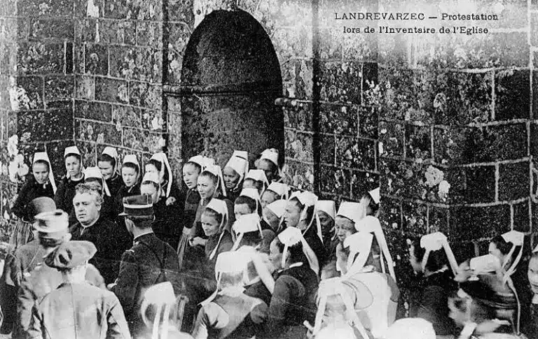 Landrévarzec : manifestation de protestation devant l'église paroissiale Saint-Guénolé lors de l'inventaire des biens d'église (vers 1906, carte postale Villard). Photographie utilisée comme illustration pour le chant La Blanche Hermine de Gilles Servat - Joseph-Marie Villard | Domaine public