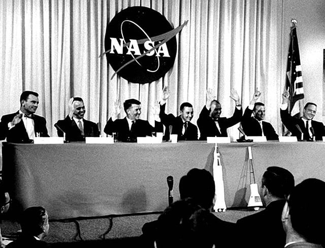 Lors de la conférence de presse du 9 avril 1959 qui a présenté les astronautes de la mission Mercury, la question suivante leur a été posée : "Qui veut être le premier homme lancé dans l'espace ?" Les sept hommes ont levé la main, Walter Schirra et John Glenn ayant levé les deux mains. De gauche à droite, Donald Slayton, Alan Shepard, Schirra, Gus Grissom, Glenn, Gordon Cooper et Scott Carpenter. | Domaine public.