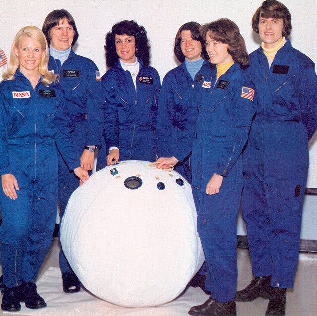 Les six premières femmes astronautes de la NASA posent avec une maquette d'enceinte de sauvetage personnelle (PRE) ou "ballon de sauvetage" dans le laboratoire des systèmes d'équipage du Centre spatial Johnson. De gauche à droite, Margaret R. (Rhea) Seddon, Kathryn D. Sullivan, Judith A. Resnik, Sally K. Ride, Anna L. Fisher et Shannon W. Lucid. 1980. | Domaine public.