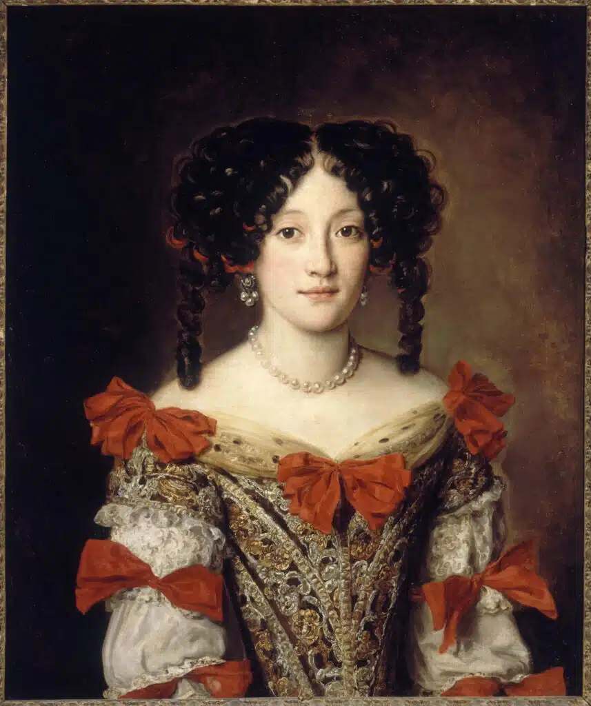 Portrait de femme représentée en buste : elle porte un costume d'époque Louis XIII, avec un corsage serré orné de rubans rouges, des boucles d'oreilles et un collier en perles et une coiffure "hurluberlu". Cette belle anonyme a été identifiée alternativement comme étant Marie-Anne Mancini - Jacob Ferdinand Voet (Musée des Beaux-Arts de la Ville de Paris, Petit Palais) | Domaine public