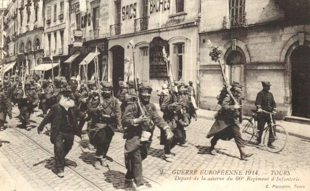 Colonne de soldats du 66e régiment d'infanterie marchant, des petits drapeaux au bout des fusils, vers la gare de Tours le 5 août 1914 au matin ; ils arrivent à Flavigny-sur-Moselle (près de Nancy) le 6 août - 66emeri (Pseudo Wikipédia) | Creative Commons BY-SA 3.0