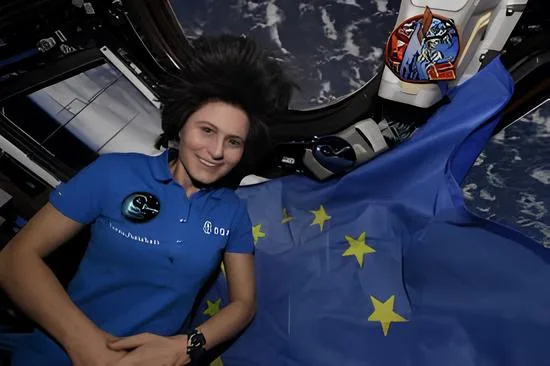 L'astronaute de l'ESA Samantha Cristoforetti dans la coupole à sept fenêtres, la « fenêtre sur le monde » de la Station spatiale internationale, avec le drapeau de l'UE - Samantha Cristoforetti | Creative Commons BY-NC-SA 4.0