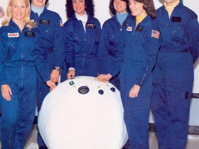 Les six premières femmes astronautes de la NASA posent avec une maquette d'enceinte de sauvetage personnelle (PRE) ou "ballon de sauvetage" dans le laboratoire des systèmes d'équipage du Centre spatial Johnson. De gauche à droite, Margaret R. (Rhea) Seddon, Kathryn D. Sullivan, Judith A. Resnik, Sally K. Ride, Anna L. Fisher et Shannon W. Lucid. 1980. | Domaine public.