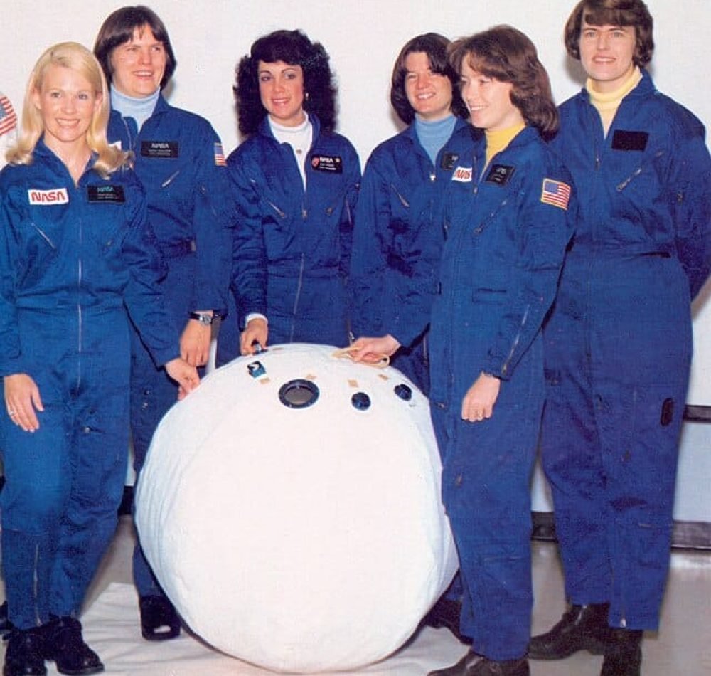 Les six premières femmes astronautes de la NASA posent avec une maquette d'enceinte de sauvetage personnelle (PRE) ou "ballon de sauvetage" dans le laboratoire des systèmes d'équipage du Centre spatial Johnson. De gauche à droite, Margaret R. (Rhea) Seddon, Kathryn D. Sullivan, Judith A. Resnik, Sally K. Ride, Anna L. Fisher et Shannon W. Lucid. 1980. | Domaine public.