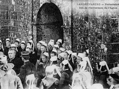 Landrévarzec : manifestation de protestation devant l'église paroissiale Saint-Guénolé lors de l'inventaire des biens d'église (vers 1906, carte postale Villard). Photographie utilisée comme illustration pour le chant La Blanche Hermine de Gilles Servat - Joseph-Marie Villard | Domaine public