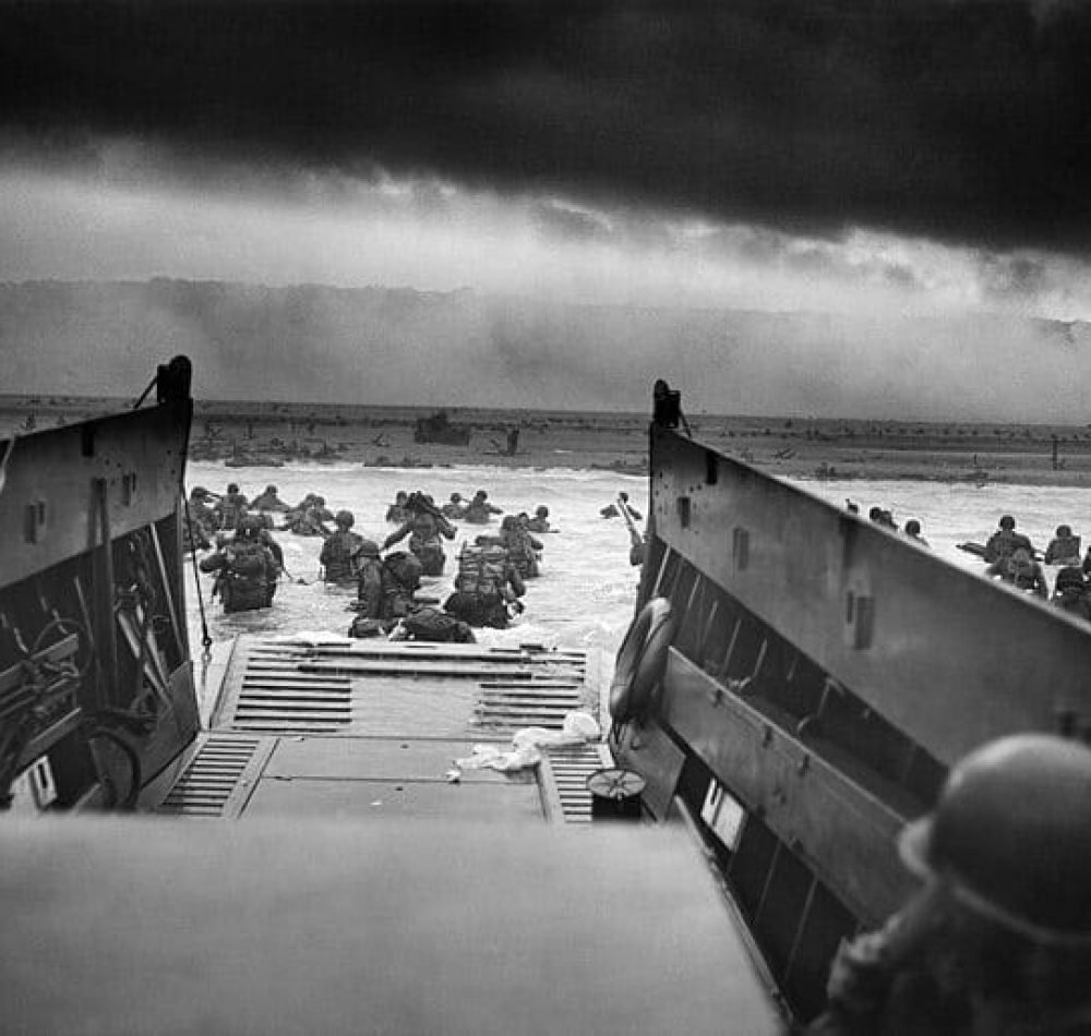 Dans les mâchoires de la mort. Un LCVP (Landing Craft, Vehicle, Personnel) des garde-côtes américain débarque des troupes de la Compagnie A, 16e Infanterie, 1re Division d'Infanterie qui pataugent sur la section Fox Green d'Omaha Beach (Calvados, Basse-Normandie, France) dans la matinée du 6 juin 1944. Lors du débarquement, les soldats américains se heurtèrent à la 352e division allemande nouvellement formée. Au cours du débarquement initial, les deux tiers de la compagnie E furent blessés - Chief Photographer's Mate (CPHoM) Robert F. Sargent | Domaine public
